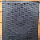 Černý reproduktor v hranatém korpusu s kovovou mřížkou z perforovaného plechu. V dolní části mřížky je bílé logo a nápis behringer. Přístroj stojí na…