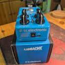 Modrý efekt pedál značky tc electronic s nápisem FLASHBACK DELAY AND LOOPER, umístěný na své modré krabici. Na horní straně jsou dva černé otočné kno…