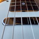 Detailní pohled na bílé tělo basové kytary s tmavým hmatníkem z dřeva. V popředí je vidět chromovaný snímač s Rounded edges. Na povrchu bílého laku j…
