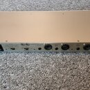 Zadní strana stříbrného rackového zařízení z kovu. Na panelu jsou nápisy CH 1 INPUT, CH 1 OUTPUT, CH 2 INPUT a CH 2 OUTPUT u příslušných konektorů. V…