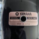 Detailní záběr na kovový štítek s nápisy, který je připevněn na černý lesklý povrch. Na štítku je logo a nápis YAMAHA, dále text MODEL SD-980RP, SER.…