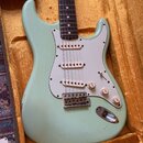 Světle zelená elektrická kytara typu Stratocaster s bílým pickguardem a třemi snímači. Tělo vykazuje výrazné popraskaní laku (crackle finish) a drobn…
