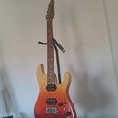 Elektrická kytara s tvarem typu superstrat v přechodovém žluto-červeném odstínu (sunburst). Nástroj má hnědý hmatník, tři černé humbuckery a černý pl…