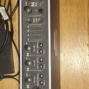 Černý audio rozhraní s kovovým stříbrným rámem a zaoblenými hranami. Na předním panelu je nápis M BOX FIT, velký ovládací knoflík a čtyři vstupní kan…