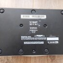 Fotografie zachycuje spodní stranu černého elektronického zařízení. Na povrchu je bílý štítek s čárovým kódem a označením (21)JM42L8038001851. Pod ní…