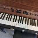Digitální klavír značky YAMAHA s dřevěným povrchem v hnědé barvě. Na ovládacím panelu jsou nápisy PITCH, DECAY, SPEED, TREMOLO INTENSITY, BALANCE, TO…
