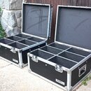 Dvě otevřené černé transportní bedny s hliníkovými hranami a vrchními víky. Vnitřní prostor každé bedny je rozdělen na šest čtvercových přihrádek a v…