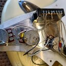 Detailní pohled do vnitřku elektroiky elektrické kytary. Jsou vidět tři potenciometry s nápisy M250kΩA a číslem 97, jeden kondenzátor a přepínač. Kab…