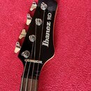 Detail hlavy černé basové kytary s nápisem Ibanez RDGR ROADSTAR. Na hlavě jsou čtyři chromované ladičky a viditelný nápis Ibanez RDGR ROADSTAR v bílé…