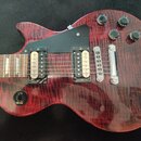 Elektrická kytara s červeným plamenovitým povrchem z dřeva a černým pickguardem. Na těle jsou dva humbuckery, čtyři černé oválné knofíky a přepínač s…