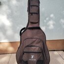 Hnědý poloměký obal na kytaru s několika zipovými kapsami. V dolní části je bílý nápis FURCH pod stylizovaným logem ve tvaru písmene F. Povrch materi…