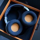 Černá velká sluchátla s vrchním obloukem a stříbrnými prvky v černém originálním boxu s oranžovým vnitřním okrajem. Sluchátka mají kulaté náušníky s…
