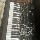 Černý elektronický klávesový nástroj s dřevěnou horní lištou. Na ovládacím panelu jsou nápisy PITCH, TINE, VIBRATO, ATTACK, SUSTAIN, BRILLIANCE, ORGA…