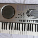 Stříbrný elektronický klávesový nástroj značky CASIO s nápisem MUSICAL INFORMATION SYSTEM. Na levé straně jsou dva kulaté reproduktory a v horní část…