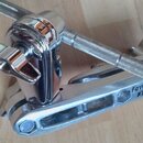 Detailní pohled na chromovaný kovový držák s přišroubovanou tyčí s texturovaným povrchem. Na boku držáku je vyražen nápis FastClaw TAMA. Povrch je le…