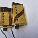 Dva elektrické snímače typu humbucker v gold povrchu. Oba mají v horní části šest viditelných šroubů a zespodu vedou šedé vodiče. Povrch je lesklý, b…