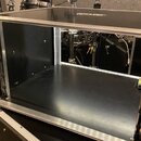 Černý transportní case s hliníkovými hranami a vrchním víkem. Vnitřní prostor je prázdný, s černým povrchem a viditelnými šrouby v rozích. V pozadí j…