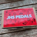Kartonová krabice s červeným obalem, na kterém je bílý nápis JHS PEDALS. Povrch krabice je doplněn různými bílými lineárními ikonami a symboly. Hrany…