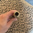 Detailní pohled na konektor audio kabelu v barvě zlata. Uvnitř konektoru jsou vidět kontakty a černé plastové vložky. Předmět drží ruka nad podkladem…