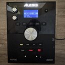 Černý elektronický modul Alesis Forge Advanced Drum Module. Na horní části jsou dva bílé oválové knoflíky s popisky MASTER VOLUME a PHONES, modrý pod…