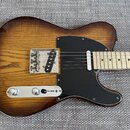 Elektrická kytara typu Telecaster s hnědým průsvitným lakem, pod kterým je vidět zrna dřeva. Nástroj má černý pickguard a světle barevný javorový hma…