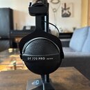 Černá uzavřená sluchátka umístěná na černém stojanu. Na vnější straně náušníku je bílý nápis DT 770 PRO 250 OHM. Povrch náušníků má zrnité provedení,…