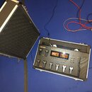 Na fotografii je kytarový procesor Boss GT-100 v bílém hliníkovém kufru s černým polstrováním. Zařízení má digitální displeje, několik ovládacích tla…