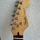 Hlavní snímek zobrazuje hlavu elektrické kytary z přírodního světlého dřeva. Na hlavě je černé logo Fender® a nápis STRATOCASTER MADE IN U.S.A. dále…