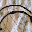 Černý kabel s několika konektory, položený na bílém textilu s květinovým vzorem. Na jednom konci je zlatý 6,3mm jack konektor a na druhém jsou dva ko…