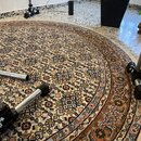 Fotografie zachycuje detaily několika chromovaných kovových stojanů umístěných na vzorovaném koberci. Na jednom z černých plastových spojů je viditel…