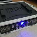 Černý transportní kufr značky GATOR s hliníkovým rámem, v němž je osazen rackový přístroj. Na předním panelu zařízení je modře svítící logo W a nápis…