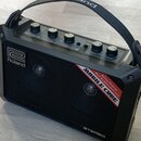 Černý přenosný stereo zesilovač s rukojetí. Na přední mřížce je bílé logo Roland a červenobílý nápis MOBILE CUBE Battery Powered Multi purpose stereo…