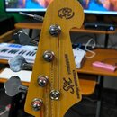 Detail hlavy basové kytary z přírodního dřeva. Na hlavě je umístěno logo SK s nápisy VTC SERIES a CUSTOM HANDMADE. Jsou vidět čtyři kovové ladičky a…