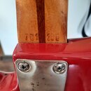 Detail zadní strany krku a spoje s korpusem červené elektrické kytary. Na dřevěném krku je vyrazen nápis 701 185. Spojení s korpusem je zajištěno kov…
