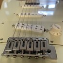 Detail elektrické kytary v krémové barvě s bílým pickguardem. Na bílém snímači je nápis "Single Coil". Kytara má chromovaný kobylník a jeden bílý ovl…