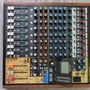 Míchací pult TASCAM Model 12 v černém provedení s dřevěným rámem. Zařízení obsahuje několik vstupních kanálů s posuvníky, otočnými knoflíky v bílé, o…