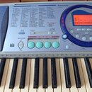 Detailní pohled na ovládací panel a klávesy elektronického klavíru značky Panasonic, model SX-KC211. Panel obsahuje displej, modré ovládací prvky a č…