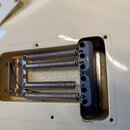 Detailní pohled na pružinový mechanismus kobylky zasazený do krmu bílé kytary. Jsou vidět čtyři kovové pružiny s nerezovým povrchem a černý plastový…