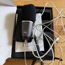 Stříbrný mikrofon s černou molovou clonou umístěný na černém stativu. Na těle mikrofonu je nápis MONITOR pod symbolem sluchátek a níže text 22040955…
