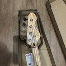 Hlava elektrické basové kytary z přírodního dřeva v kartonovém obalu. Na hlavě je svisle napsáno „Vintage REISSUED Series“ a v horní části je vidět l…