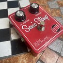 Červený efekt pedál s nápisy Sonic Stomp a SONIC MAXIMIZER. Na horní straně jsou dva černé ovládací knoflíky s kovovými vršky a doprovodné popisky LO…