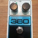 Bílý kytarový pedál s nápisy nano looper a 360 v modrém rámečku. V horní části jsou dva černé oválové knoflíky s popisky LEVEL a LOOP, nad nimi nápis…