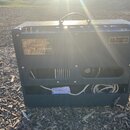 Zadní strana kytarového komba v tmavě modré barvě s texturovaným povrchem. Na levé straně je stříbrný štítek s nápisy Deluxe, Fender a CE, vpravo je…
