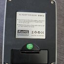 Záběr na zadní stranu černého efektpedálu v hliníkovém šasi. Na bílém štítku je nápis AC ADAPTER DC9V, varovné texty ohledně baterie a označení RoHS,…