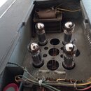 Fotografie zachycuje vnitřek elektronického zařízení v šedém obalu. Uvnitř jsou vidět čtyři zapojené elektronky, transformátor a různé elektrody s ka…