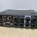 Zadní strana černého elektronického zařízení s kovovým rámem. Jsou zde viditelné konektory, včetně dvou portů pro síťový kabel, D-Sub konektoru s náp…