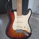 Elektrická kytara typu Stratocaster s barevným přechodem těla od černé přes červenou k žluté. Nástroj má bílý pickguard, tři snímače s bílými krytkam…