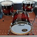 Sada bubnů v tmavě červeném, vysoce lesklém provedení s imitací dřeva. Na každém z trzech korpusů je viditelné zlaté logo „Mapex“. Přední blana basov…