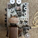 Fotografie zachycuje vnitřní pohled na elektronický přístroj s otevřeným šasi. Jsou vidět různé komponenty, včetně několika velkých válcových kondenz…