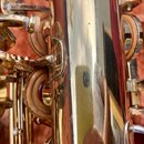 Detailní záběr na zlatý kovový povrch saxofonu s viditelnými klapy a polštáři. Povrch je znečištěný prachem a vykazuje drobné škrábance a opotřebení.…